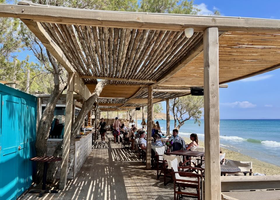 People lounge at a thatched roof beach bar on the sand