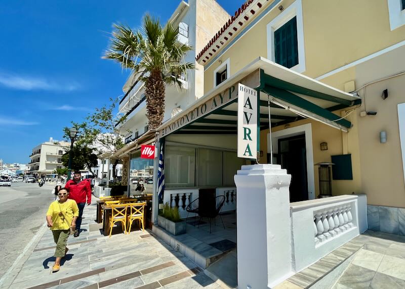 View of the exterior entrance of a city hotel in a Greek town, with pedestrians walking by