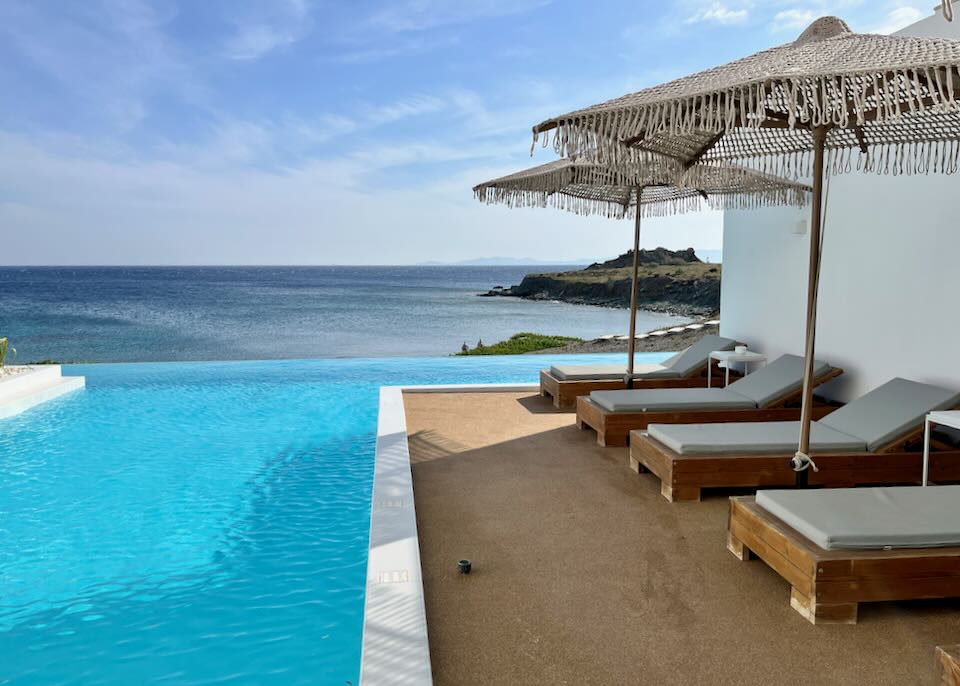 Sun beds with woven umbrellas next to an infinity pool overlooking the blue sea