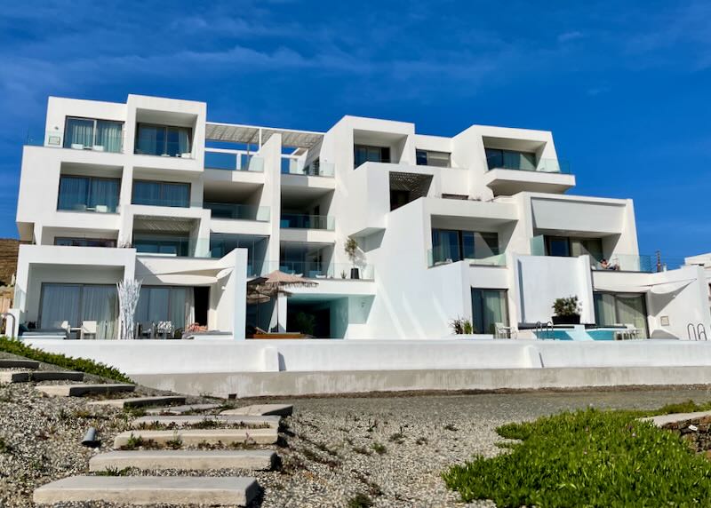 White boxy hotel with a swimming pool and steps leading into the sand