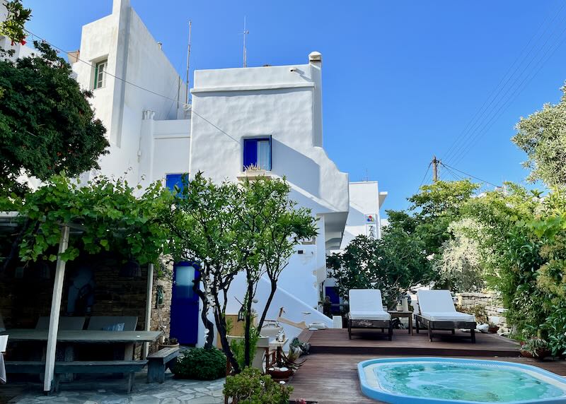 White Cycladic hotel with blue shutters next to a small pool terrace