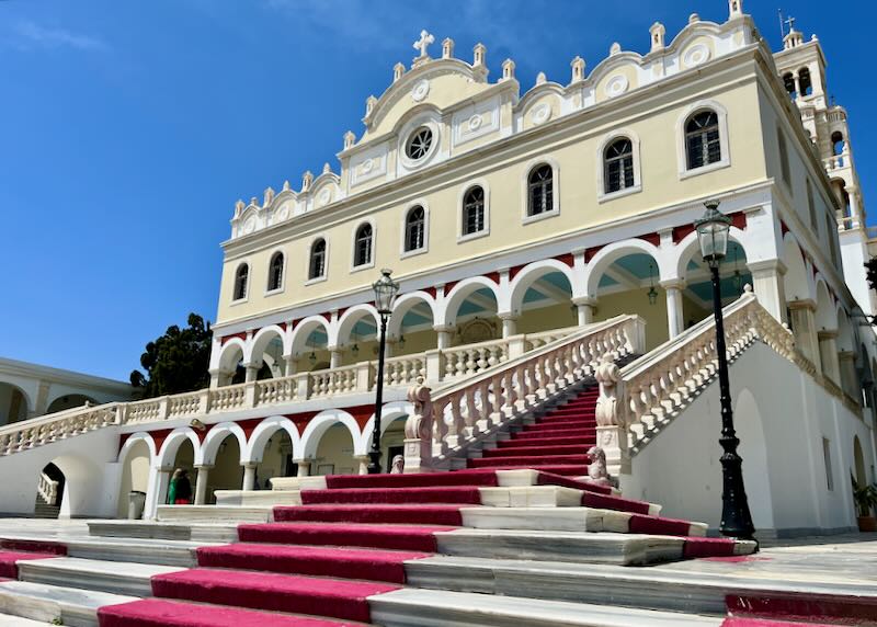 Cream colored church with arched colonnade, seen from the bottom of a set of stairs lined with a red carpet