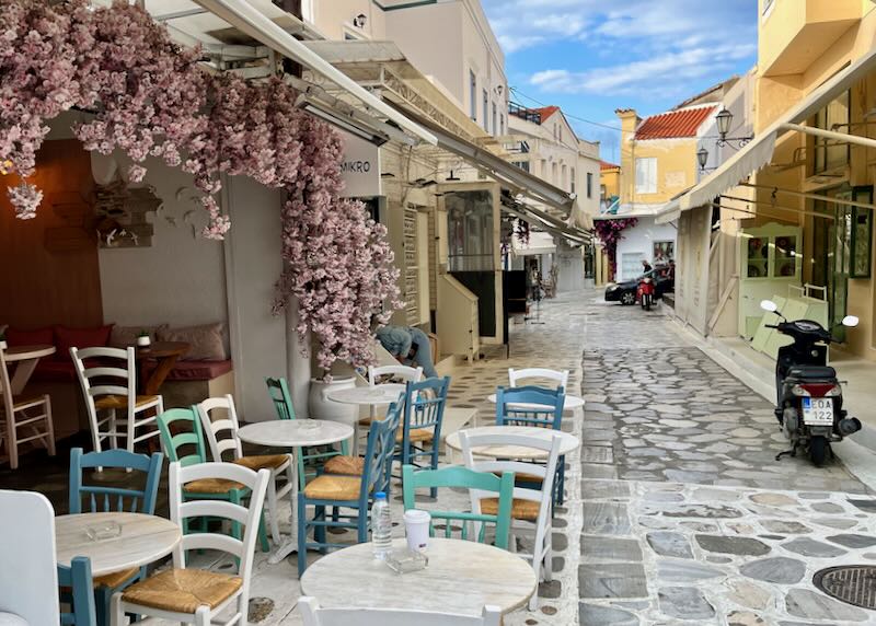 Colorful cafe tables shaded by bougainvillea on a narrow stone street