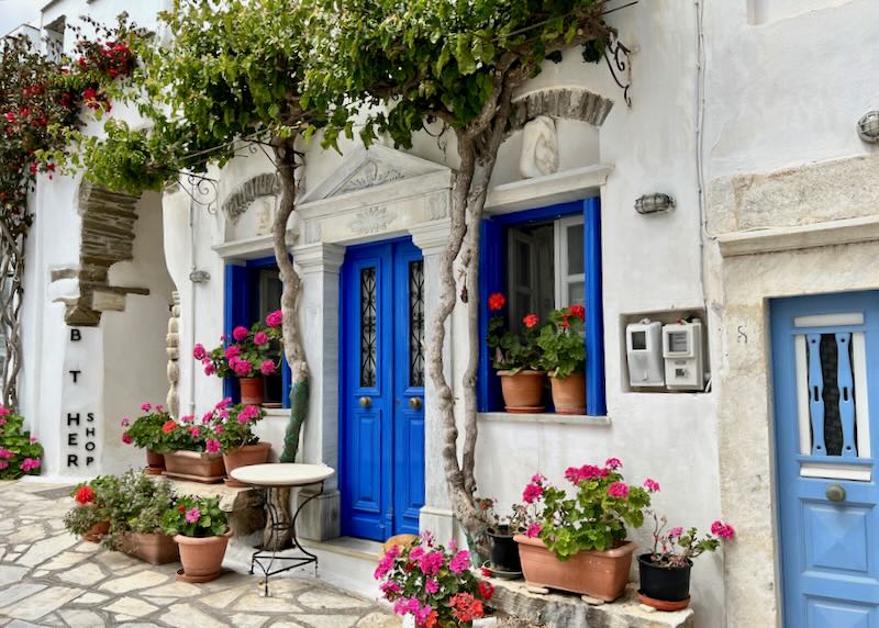 White stone building with blue doors and shutters, with flowers in front