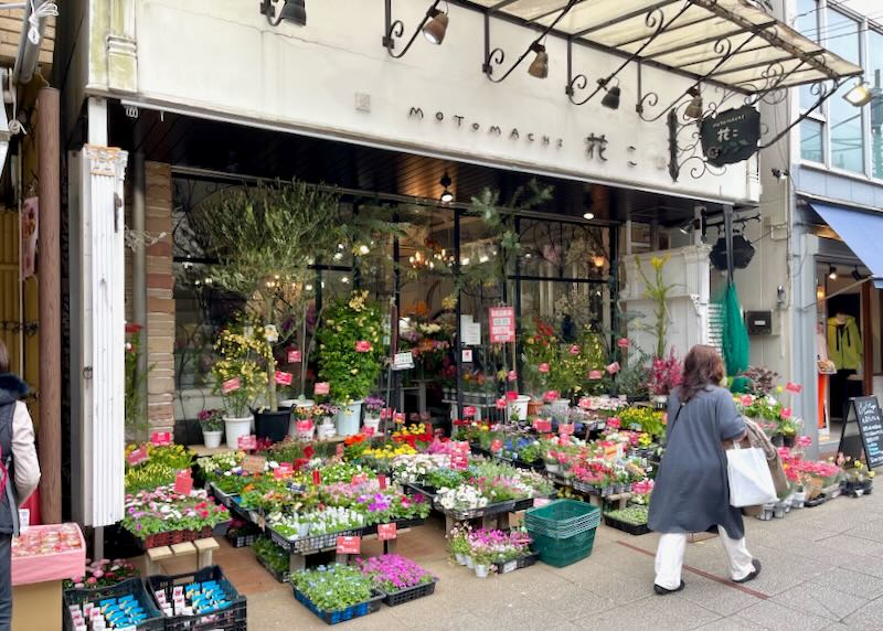 A woman walks past a flower boutique selling blooming plants.