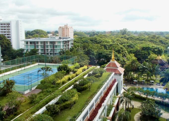 A tennis court sits on the roof overlooking lush green trees.