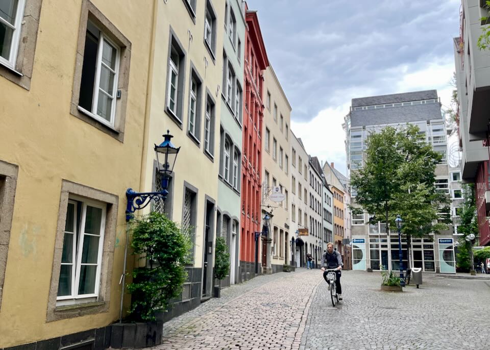 A man bikes over narrow cobbled streets past colorful buildings.
