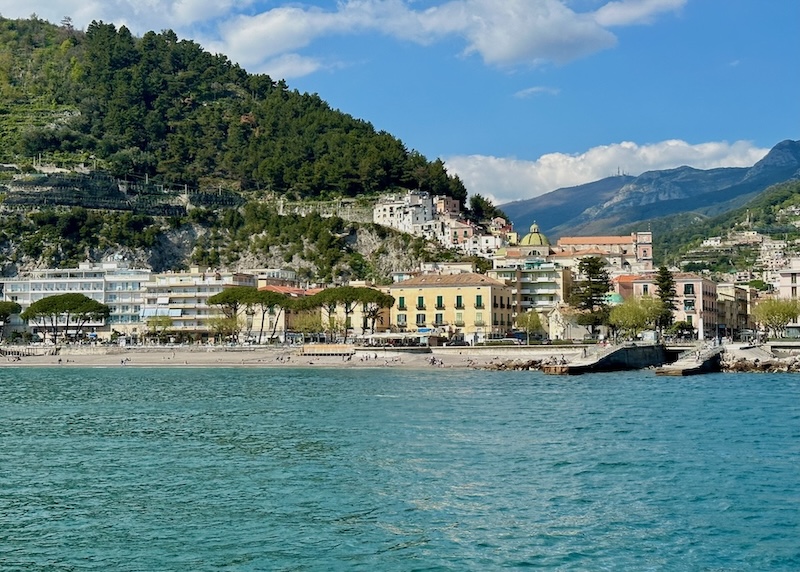 View of Maiori from the sea with the church dome, beach, and a row of multi-story buildings.