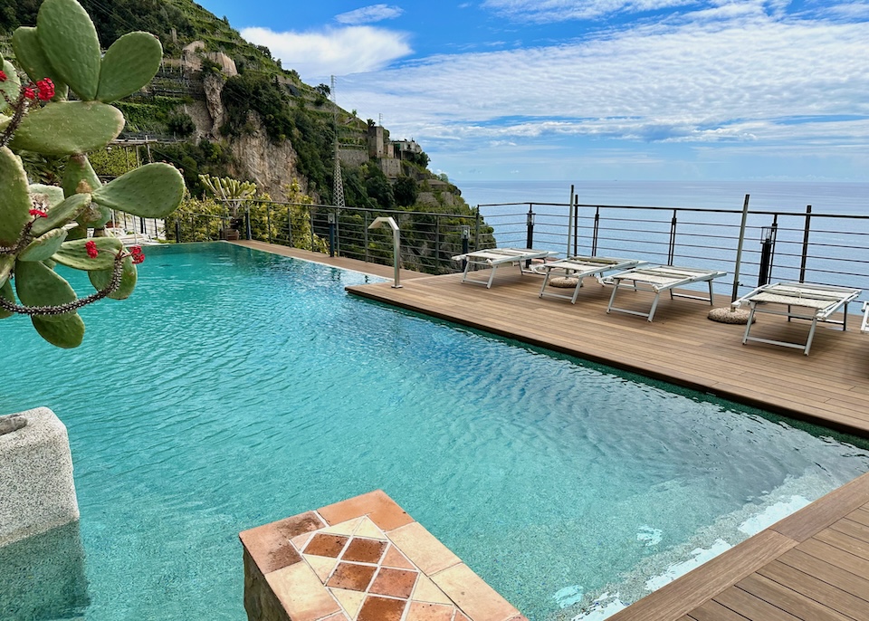 A pool and wooden deck overlooking the sea shaded by a cactus at Botanico San Lazzaro in Maiori on the Amalfi Coast