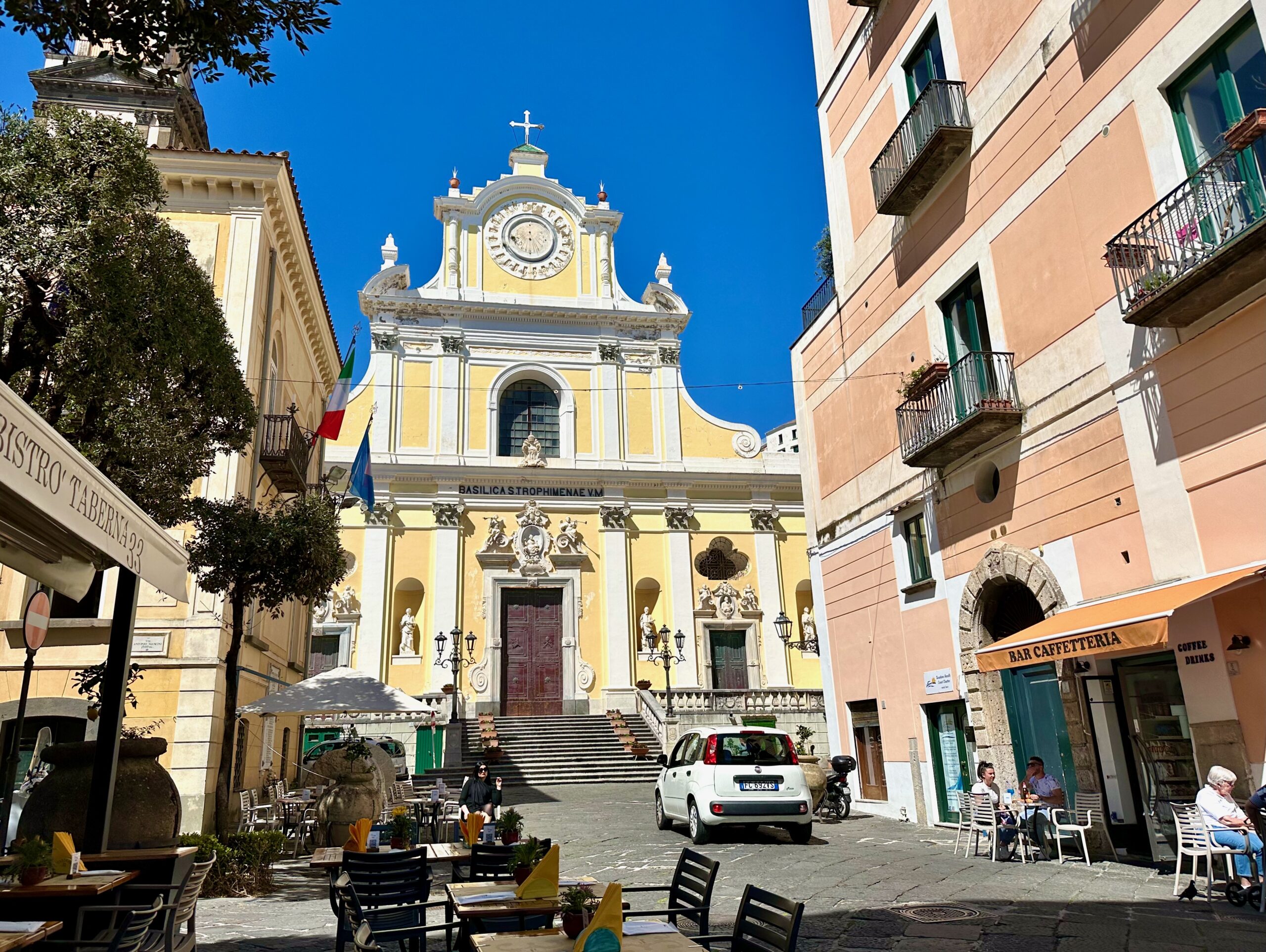 Basilica with a yellow and white facade and restaurants on either side of the street in Minori on the Amalfi Coast.