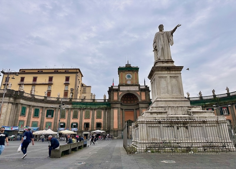Statue of Dante Alighieri in a piazza with a historic, semi-circular building behind in the Montecalvario neighborhood of Naples, Italy