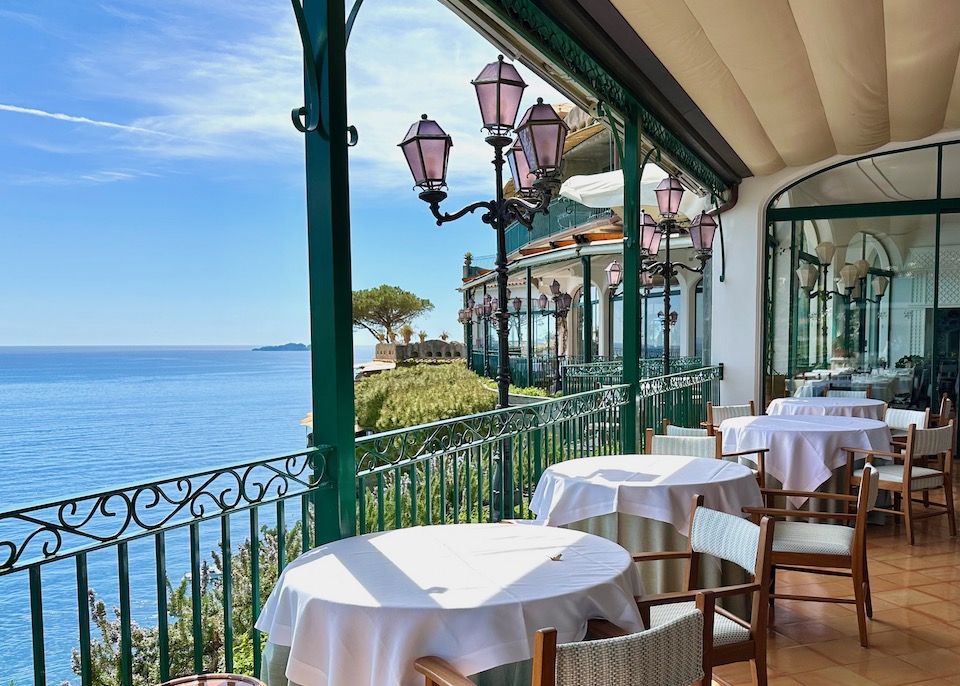 Sea view from the terrace of a hotel restaurant with white cloth-covered tables on a terrace and antique lamps