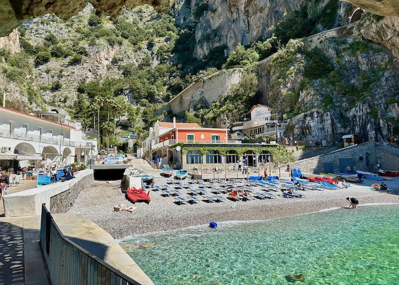 A small beach tucked at the base of a cliff with a beach club and restaurants in Praiano on the Amalfi Coast