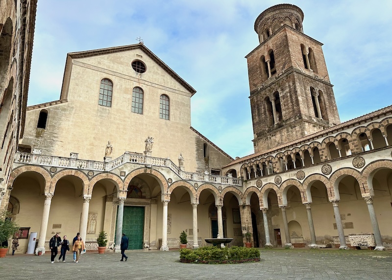 Stone facade and bell tower with an ornate, wraparound arcade in the courtyard of the Duomo of Salerno.