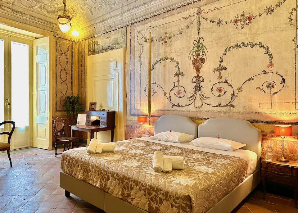 Walls richly frescoed in a dainty floral style in a suite with a terracotta floor and antique furniture at Casa Santangelo in Salerno, Italy