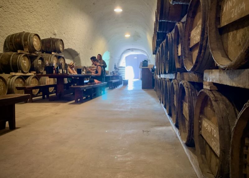 A couple tastes wine in a vaulted cave cellar lined with barrels