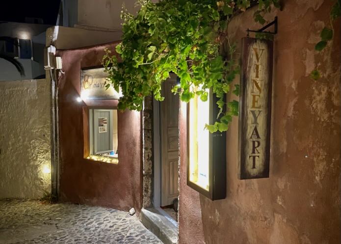 Open doorway, hung with vines and with light streaming out onto a cobbled narrow alley.
