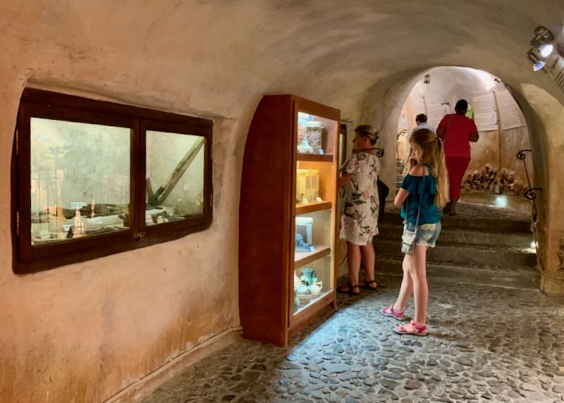 People pause to look at a museum display in whitewashed stone cave passageway 