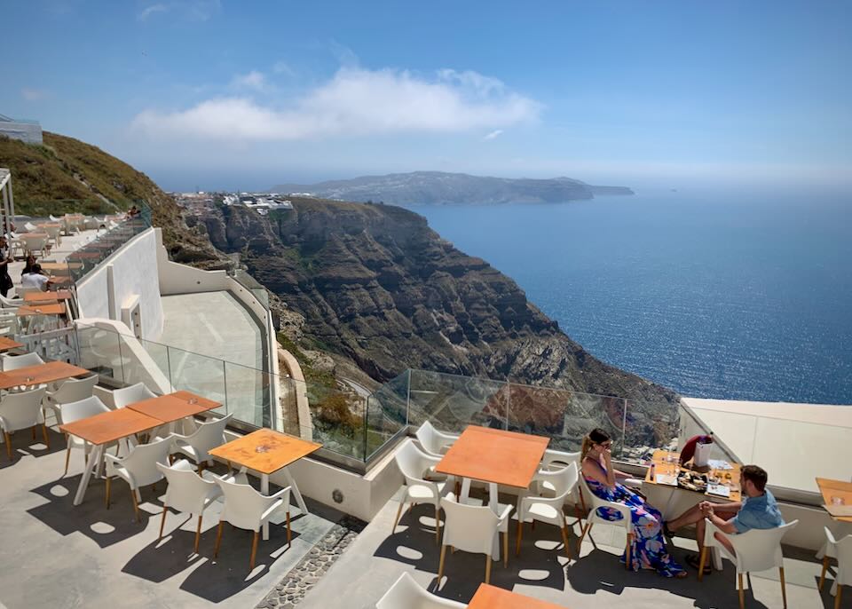 People taste wines at a table next to a picturesque caldera cliff