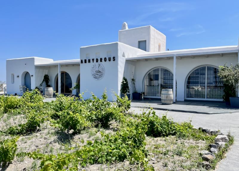White, Cycladic-style building with arched colonnade, set in a vineyard.