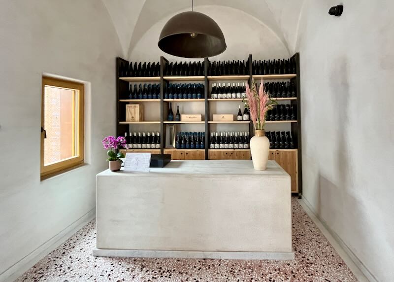 Reception desk in a vaulted stone room, backed by shelves of wine.  
