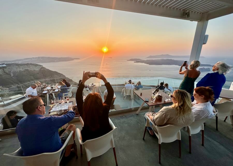 People take photos of a beautiful caldera sunset from a wine-tasting terrace