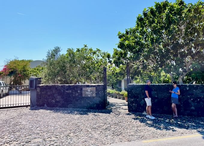 Two people wait outside a stone gate to a winery