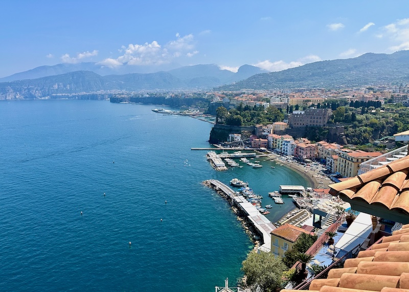View over a small marina, beach, red tile roofs, and green mountains with the ferry port in the background in Sorrento, Italy