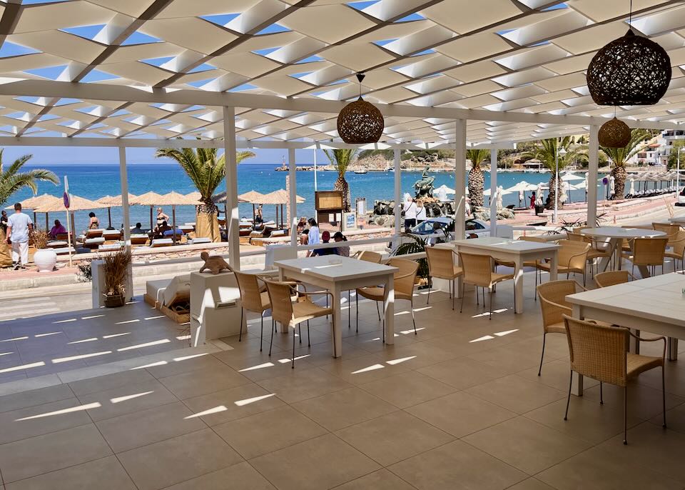 Covered terrace with white tables and rattan pendant lights, open to the beach.