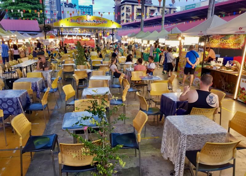Plastic yellow chairs and tables line a street at a food market.