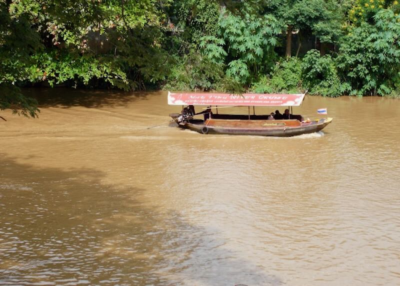 A small wood boat with a red canopy moves passengers along a brown river.