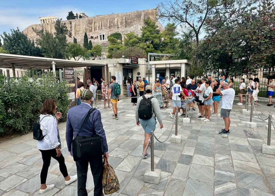 People walk to a ticket booth under the Athens Acropolis