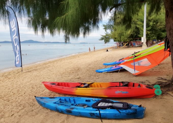 Colorful kayaks rest on the beach under a tree.