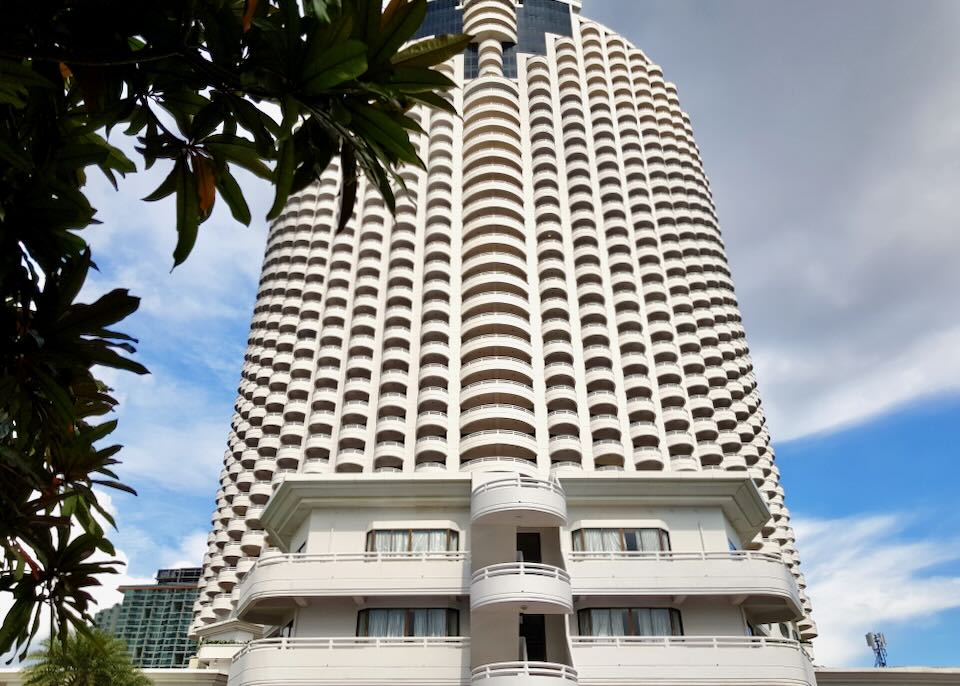 A tall white hotel with curved balconies stands tall.
