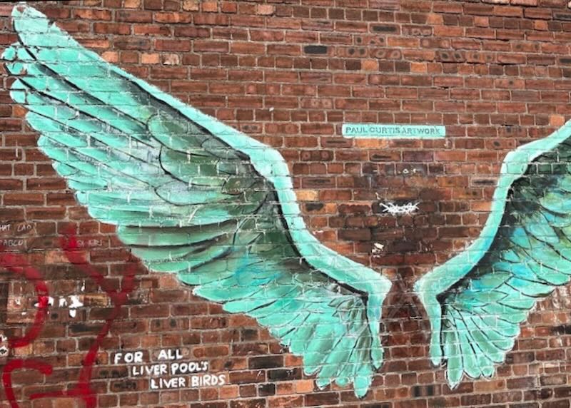 Mural on a red brick wall of giant green bird wings