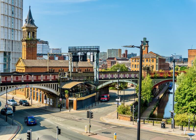 Manchester United Kingdom Deansgate railway station with a view over a canal. Cars are visible on the streets.