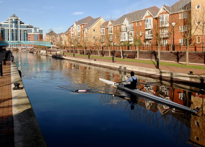 A single crewed boat sculling along the ship canal in Manchester, England