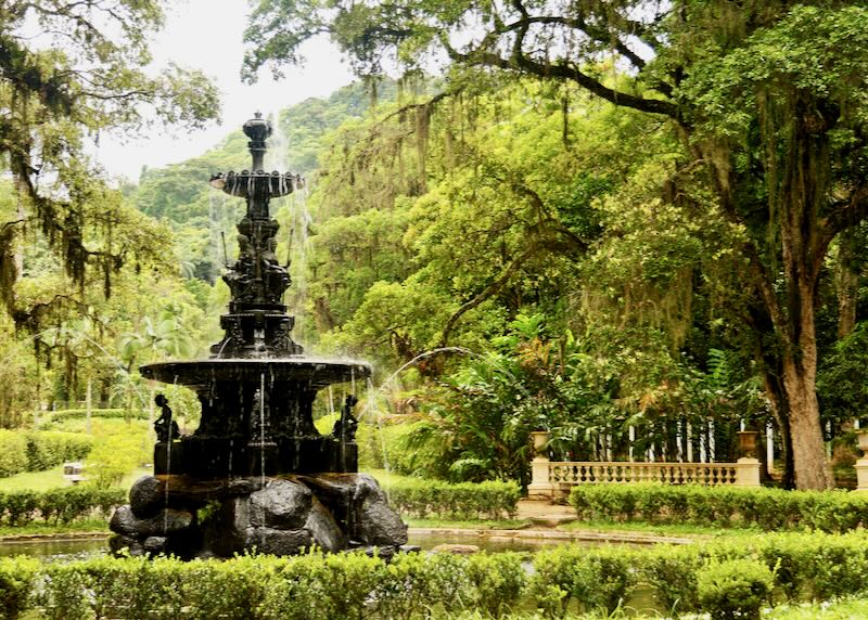 Stone water fountain surrounded by lush green foliage.