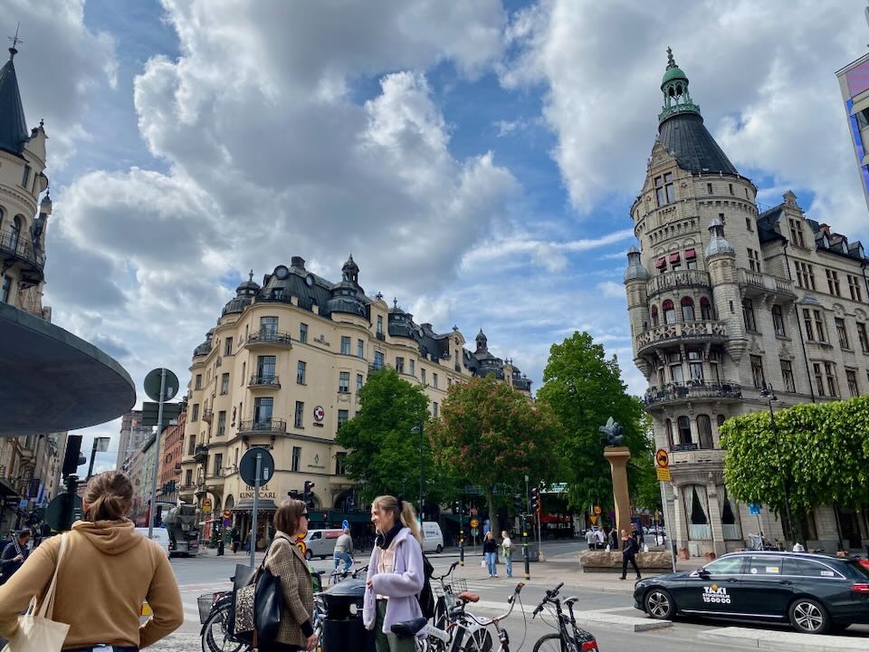 Pedestrians stop to talk on a corner surrounded by large ornate buildings