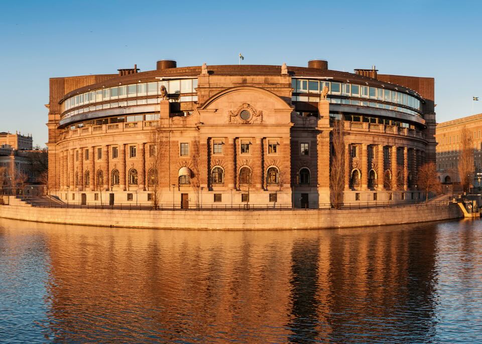 Golden sunlight of sunset illuminating the historic stone and modern glass additions of the Riksdaghuset, home to the Swedish Riksdag parliament.