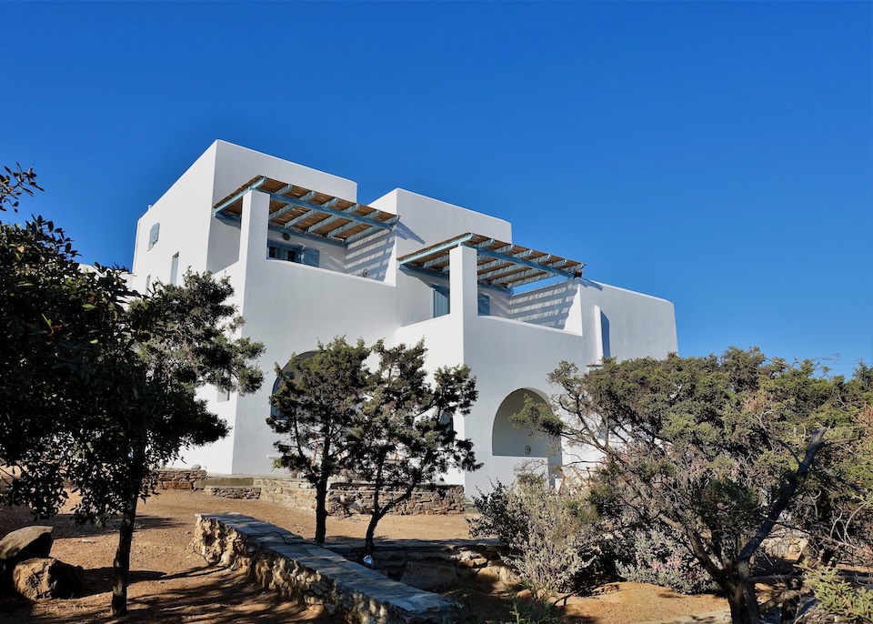 Whitewashed, cubic exterior of Oliaros Seaside Lodge surrounded by trees in Antiparos