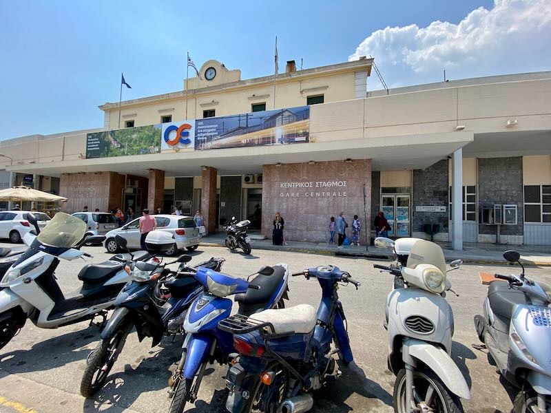 Exterior view of the front of a train station, with a row of motorbikes parked in front.