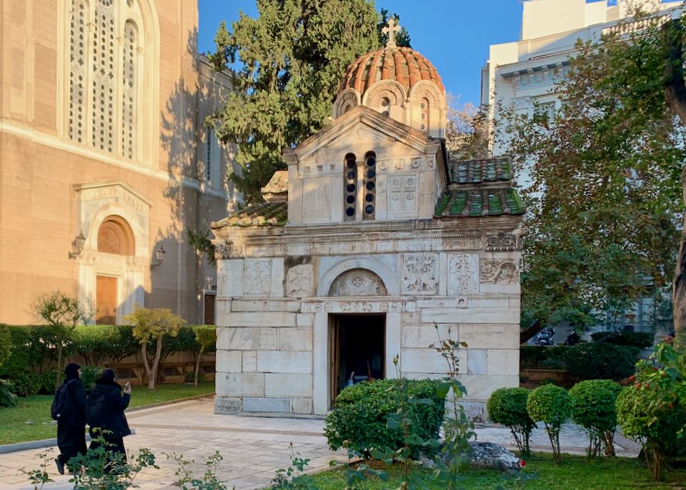 Two nuns dressed in black walk toward the entrance of a small Byzantine church.