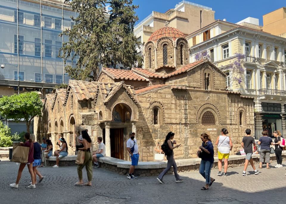 People walk by a Byzantine era church set amid modern buildings. 