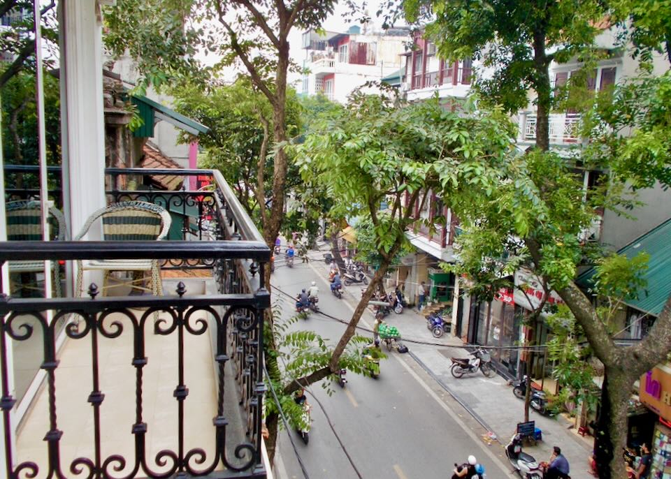 A black iron fenced balcony overlooks a busy street in Hanoi, Vietnam.