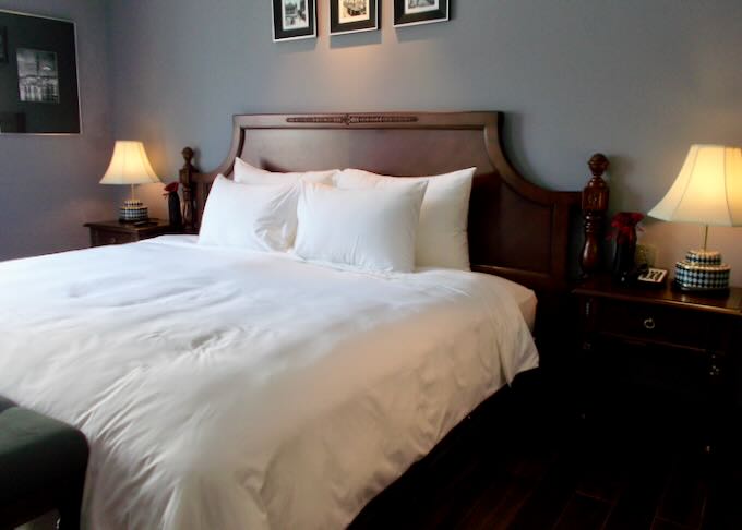 A wooden bed frame holds a white linen comforter.