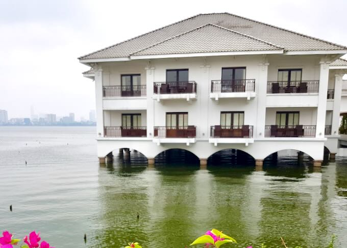 a hotel sits on stilts over a green lake.
