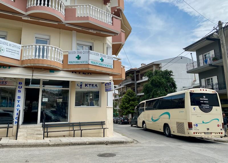 Small corner bus station with bus waiting in front, with signage in Greek