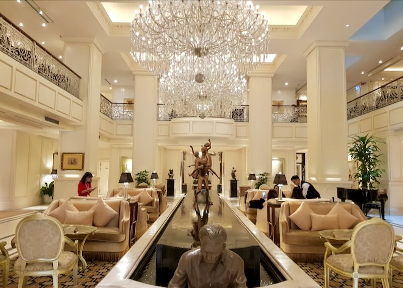 A crystal chandelier hangs above velvet loveseats and a sculpture fountain.