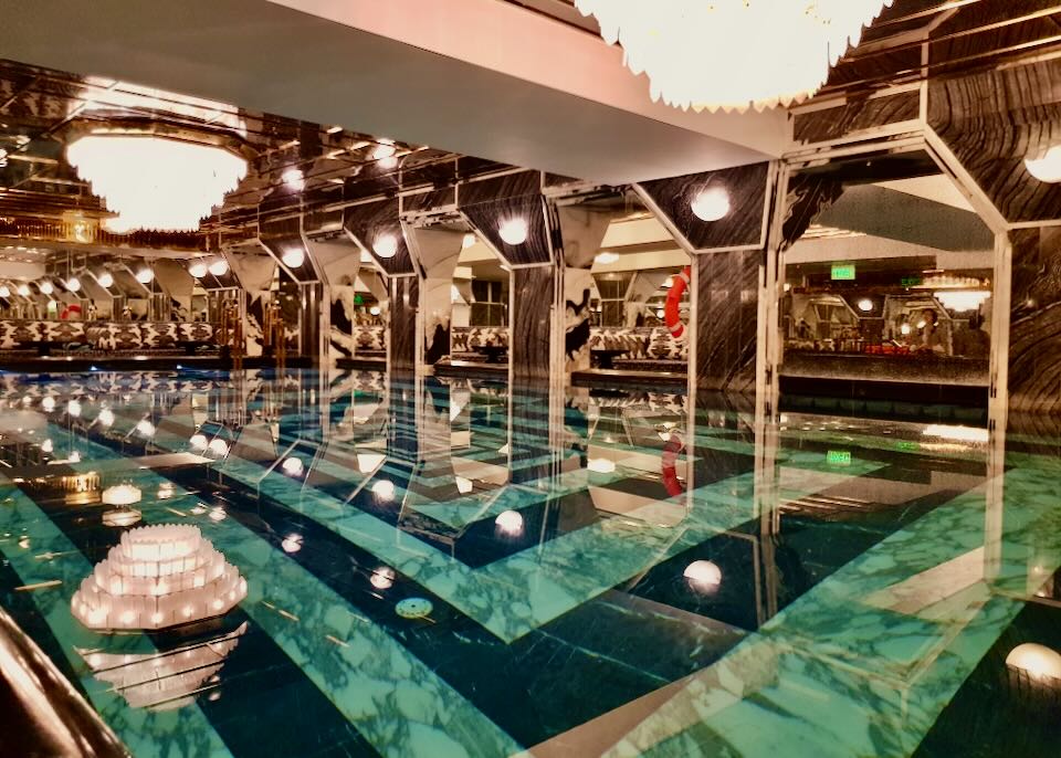 A black and white marble indoor pool with chandeliers and mirrors.